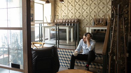 verzweifelter Gastronom sitzt in seinem leeren Restaurant/Café/Lokal