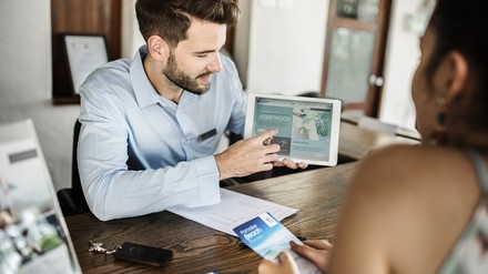 Tablets und App-Lösungen finden auch in der Hotellerie immer häufiger Anwendung zur Unterstützung der Kundenbeziehungen. (Foto: ©Rawpixel Ltd./stock.adobe.com)
Rezeptionist im Hotel zeigt einer Frau etwas auf einem Tablet