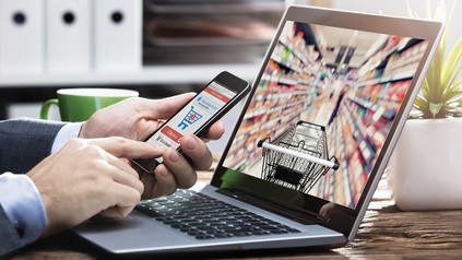 Ein Mann tippt vor einem Laptop auf seinem Handy um etwas zu bestellen