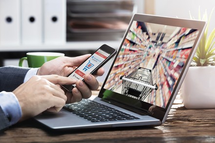 Ein Mann tippt vor einem Laptop auf seinem Handy um etwas zu bestellen