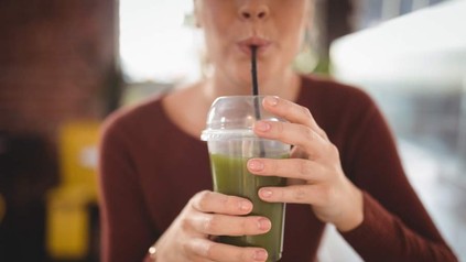 Eine Frau trinkt mit einem Trinkhalm aus einem Plastikbecher