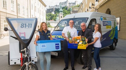 Vier Personen präsentierenWaren vor einem Metrotransporter und einem Lieferfahrrad