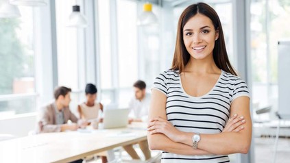 Eine junge Frau steht lächelnd vor einem Besprechungstisch in einem modernen Büro