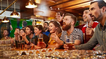 Viele Menschen sitzen in einer Bar und jubeln mit Bier in den Händen