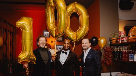 Drei Männer in Anzügen stehen nebeneinander, halten Luftballons, L’Osteria