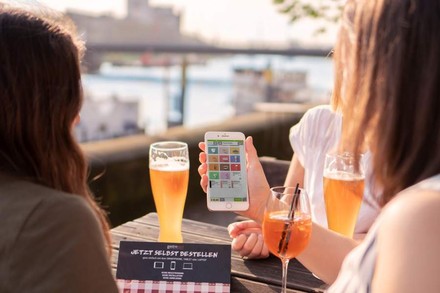 Junge Frauen an einem Tisch mit Bier und Sprizz, die auf ein Smartphone blicken
