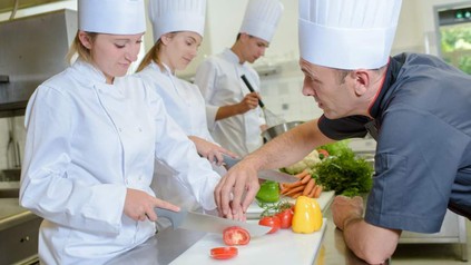 Chef erklärt Azubi, wie man eine Tomate schneidet