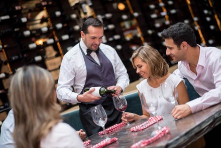 Wirt schenkt Gästen Rotwein ein