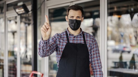 Gastronom mit Schutzmaske hebt warnend den Zeigefinger