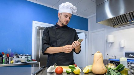 Ein Koch in der Küche blickt auf sein Smartphone