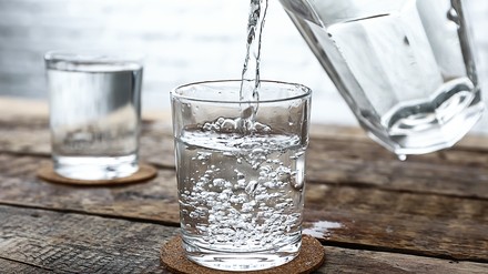 Jemand gießt Wasser in ein Glas
