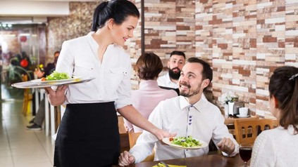 Eine freundliche Servicekraft serviert lächelnden Gästen Salate