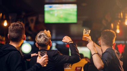 Jubelnde Fans sehen sich in einer Kneipe ein Fußballspiel mit Bier in der Hand an