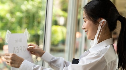 Asiatische Kellnerin hängt ein Geöffnet-Schild an die Restaurant-Tür