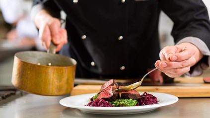 Ober mit Kochtopf gießt Sauce auf Fleisch