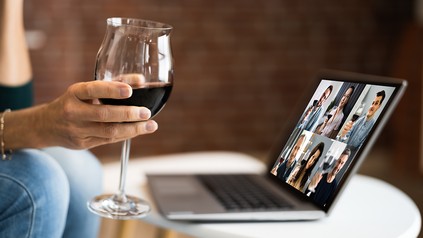Nahaufnahme einer Frau, die mit einem Rotweinglas vor dem Laptop sitzt und an einer Online-Weinverkostung teilnimmt