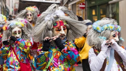 Ein Karnevalszug in Basel mit Menschen, die Hippikostüme und große Masken tragen