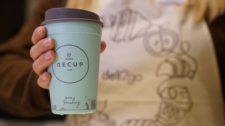 Eine Frau hält einen Recup-Pfandbecher in der Hand