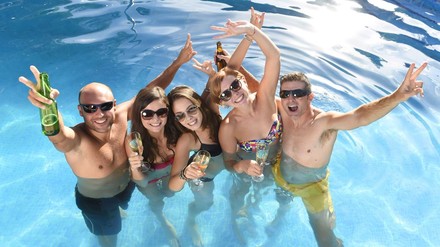 Junge Urlauber in einem Pool mit Bier und Sektglas in der Hand