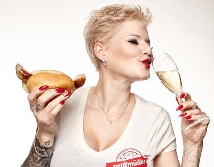 Frau trinkt Sekt und hat Bratwurstsemmel in der Hand