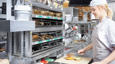 Eine Mitarbeiterin in der Küche an einem professionellen Küchengerät