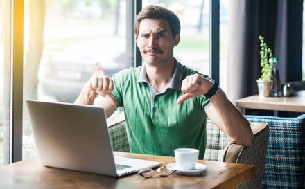 Mann sitzt vor Laptop und macht Daumen-runter-Geste.