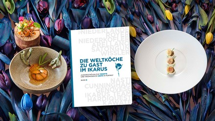 Band sechs der Buch-Reihe „Die Weltköche zu Gast im Ikarus“ liegt zwischen zwei Signature Dishes auf einem Tisch voller Blumen
