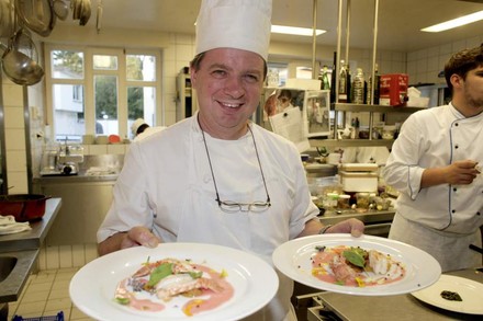 Spitzenkoch Jean-Marie Dumaine mit zwei Tellern in der Hand in seiner Küche