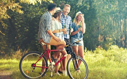 Freundesgruppe mit einem Fahrrad in der Natur trinkt Bier aus Flaschen.