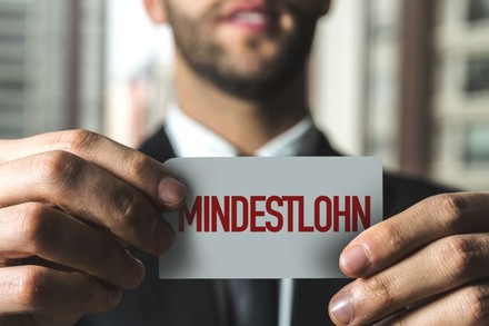 Mann hält Zettel mit Inschrift „Mindestlohn“ in den Händen