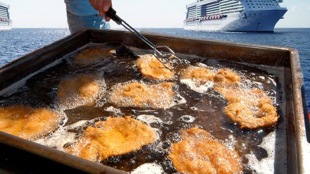 EIne Wanne voller Frittierfett vor einem Kreuzfahrtschiff