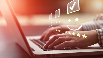 Nahaufnahme von Frauenhänden, die auf einem Laptop tippen, darüber grafische Symbole für eine Online-Bewertung