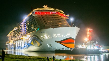 Ein beleuchtetes AIDA-Schiff bei Nacht.