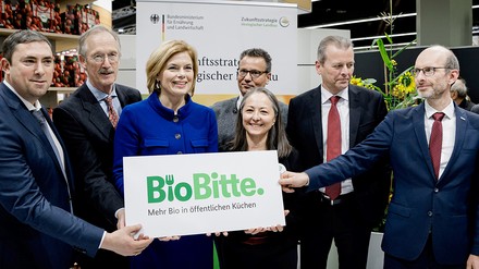 Julia Klöckner und weitere Politiker auf der Messe Biofach halten ein Kampagnenschild mit dem Schriftzug „BioBitte“