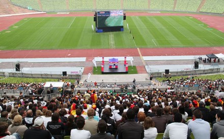 Ein gut besuchtes Fußballstadion auf dessen Rasen eine große Leinwand für Public Viewing aufgebaut ist