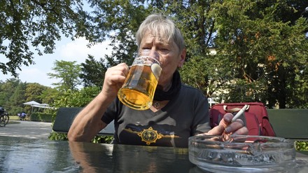 Ältere FRau sitzt mit Bierglas und Zigarette im Gastgarten