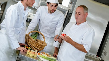 Ein Koch unterrichtet zwei Lehrlinge in Lebensmittelkunde