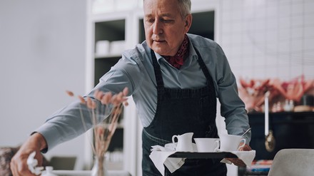 Älterer Mann, der in einem Restaurant oder Café arbeitet und den Tisch deckt