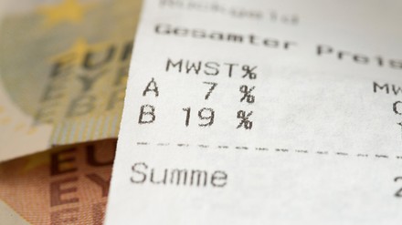 Nahaufnahme eines Kassenbons mit Blick auf die Mehrwertsteuer, im Hintergrund liegen Euro-Geldscheine