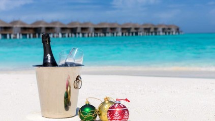 Ein karibischer Strand, auf dem ein Sekteimer und Christbaumkugeln stehen.