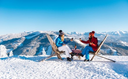 2 Frauen sitzen auf einer Skipiste in Liegestühlen und genießen ein Glas Wein