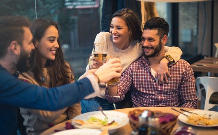 Freundesrunde an einem Esstisch, die mit Bier anstoßen