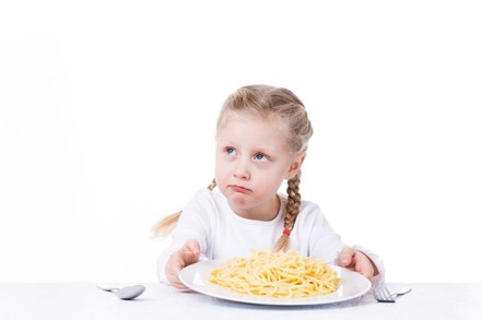 Mädchen mit Teller voller Spaghetti blickt traurig nach oben