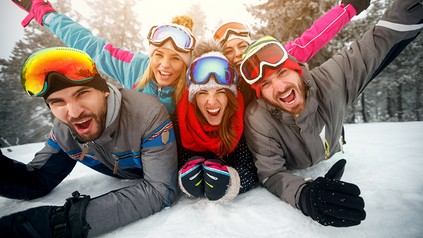 Eine Gruppe Skifahrer liegt auf dem Boden und winkt fröhlich in die Kamera