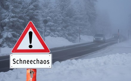 Warnschild „Schneechaos“ vor einer Winterlandschaft