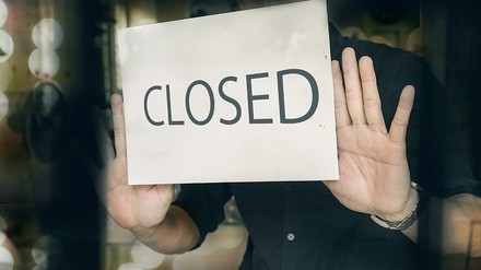 Ein Mann bringt ein „Closed“-Schild an die Glastür seines Restuarants an
