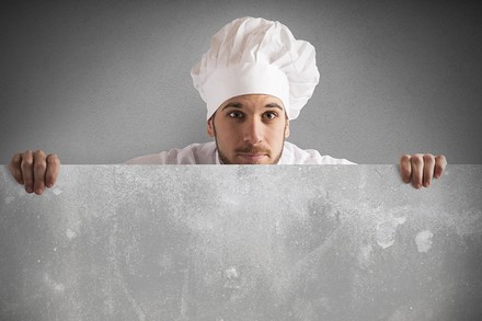 Ein Koch, der vorsichtig hinter einer Mauer hervorschaut