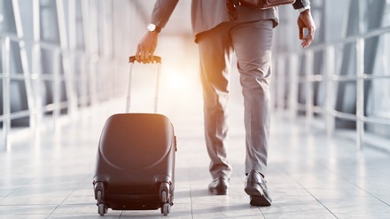 Mann im Anzug zieht Rollkoffer den Gateway entlang