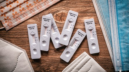 Coronatests auf dem Tisch umringt von Masken