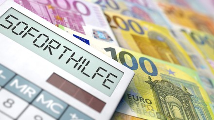 Taschenrechner in dessen Display „Soforthilfe“ steht, im Hintergrund liegen Euro-Geldscheine